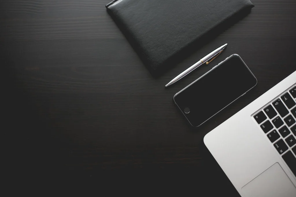 Dunkler Tisch mit Laptop, Stift und Smartphone